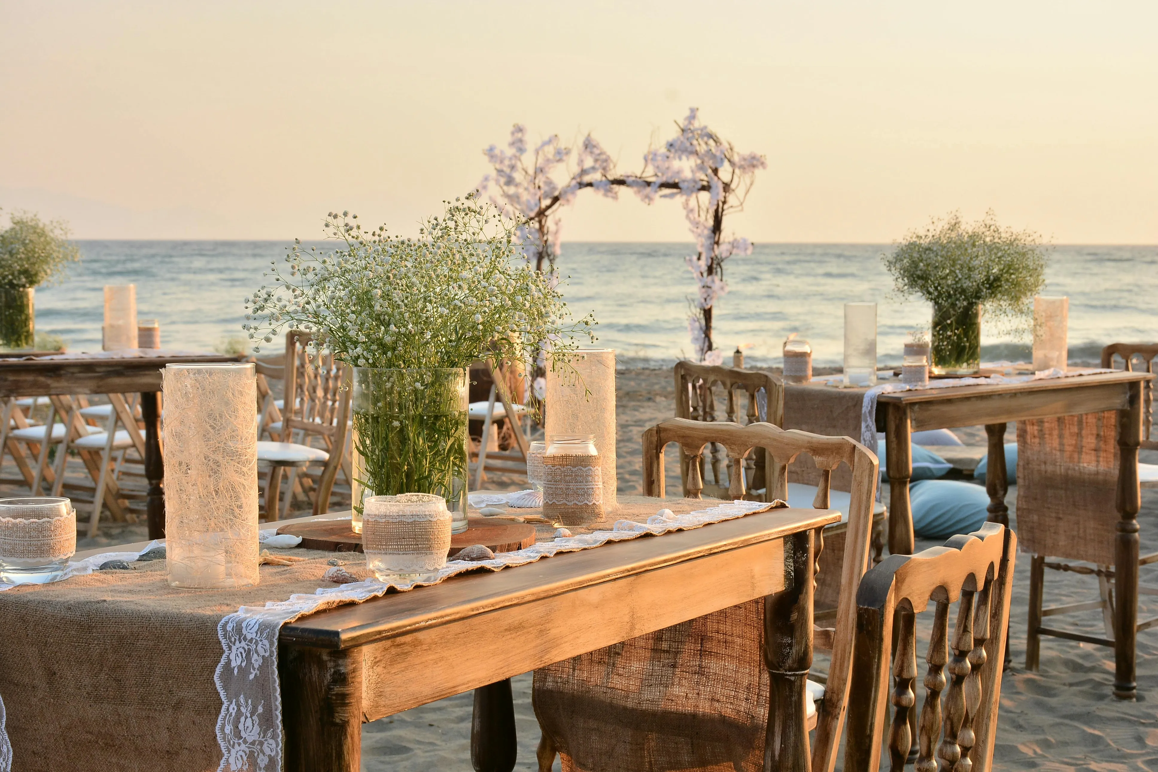Gün batımında romantik kumsal düğün dekorasyonu, beyaz şemsiyeler ve deniz manzarası ile bohem tarzı düğün organizasyonu