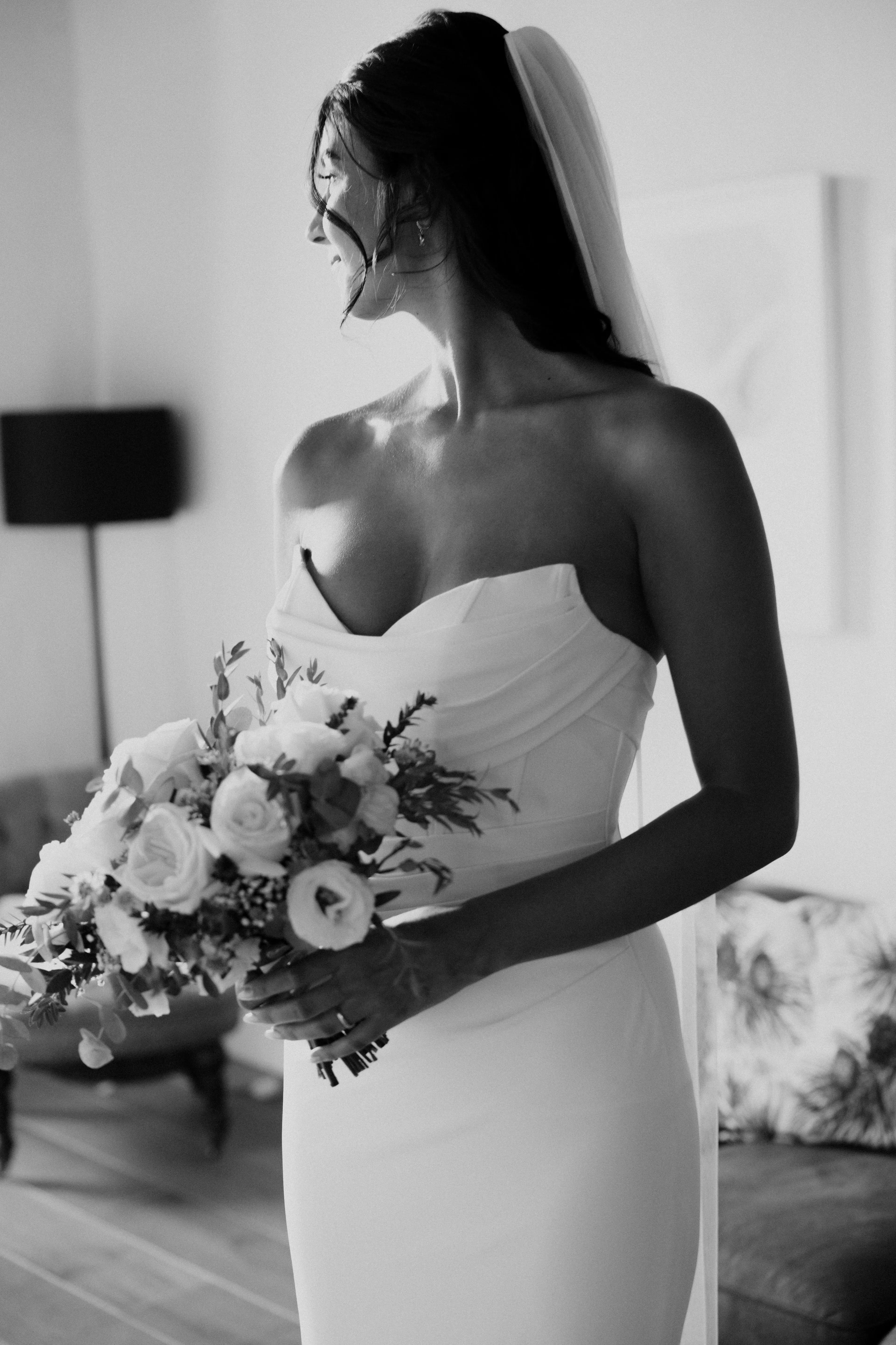 Modern minimalist straplez gelinlik, mikado saten kumaş ile düz göğüs hattı tasarımı, beyaz mermer zemin üzerinde şık sunum fotoğrafı, profesyonel stüdyo ışıklandırması